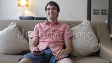 年轻的帅哥正在看电视，正坐在沙发上微笑
